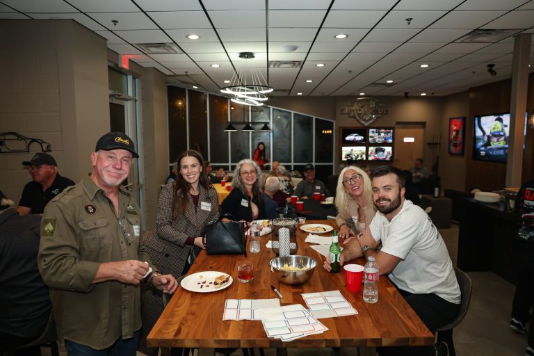 Group of adults seated around a long wooden table, dining and chatting in a modern event space.