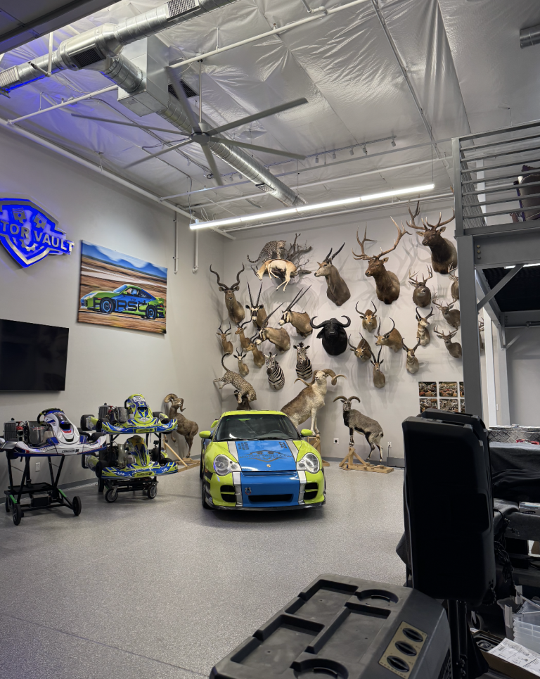 Bright showroom with a lime-green and blue sports car, go-karts on the left, and a wall of mounted animal heads as a display backdrop.